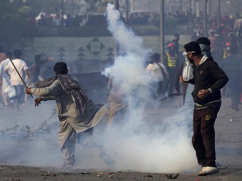 A supporter of former Prime Minister Imran Khan hurls back a tear gas shell fired by riot police officers to disperse them during clashes, in Lahore, Pakistan, Wednesday, March 15, 2023. K.M. Chaudary/AP